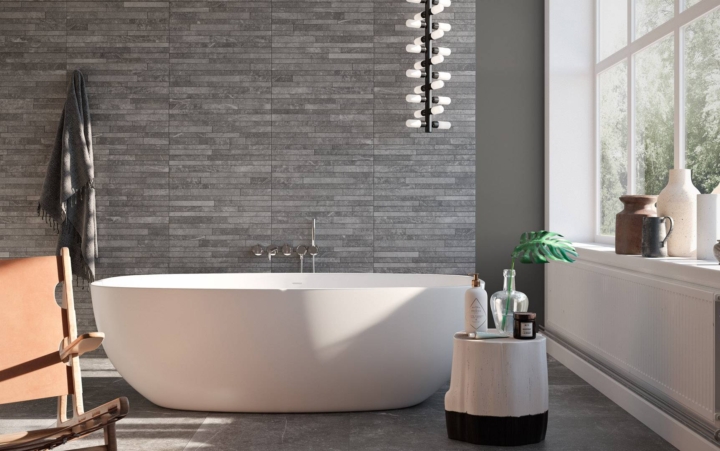 Modern bathroom with white tub, gray tile wall, large windows, and minimalist decor